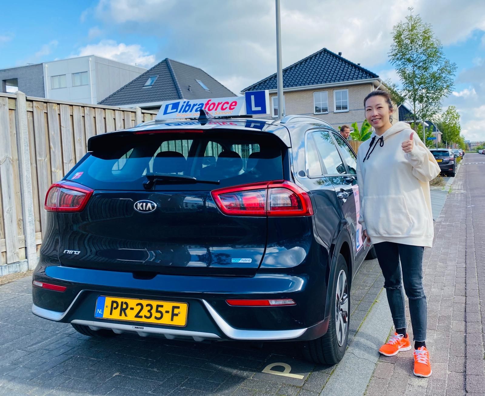 Een geslaagde leerling bij de donkerblauwe lesauto van LibraForce