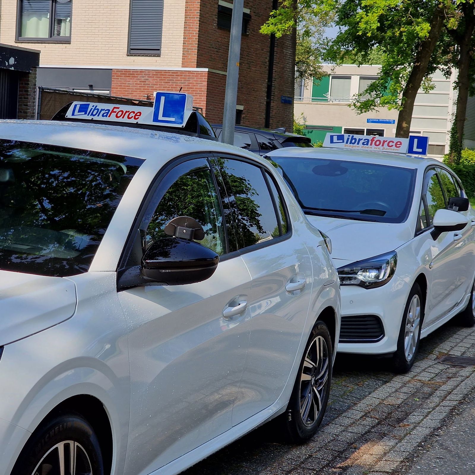 Twee witte lesauto's van LibraForce naast elkaar, met het lesbord op het dak